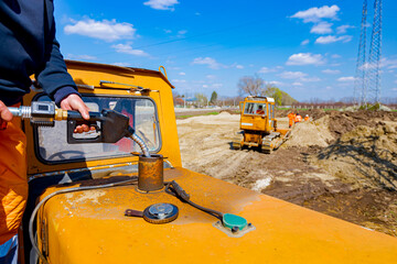 Hand holding handle fuel nozzle to refuel, petrol is pouring into the tank of an industrial...