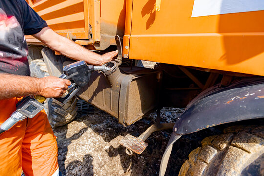 Hand holding handle fuel nozzle to refuel, petrol is pouring into the tank of an industrial mechanization