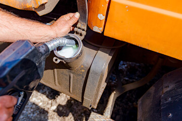 Hand holding handle fuel nozzle to refuel, petrol is pouring into the tank of an industrial mechanization