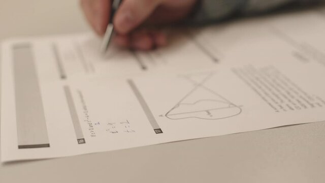 Locked-down of hand of unrecognizable student solving mathematical problems, writing with pen on paper on test