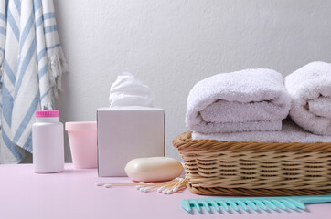 Closeup of items for baby bathing.Stack of soft towels,soap,paper napkins,cream, powder,comb on the pink desk against white wall