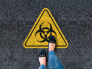 legs in shoes standing on asphalt road and biohazard sign
