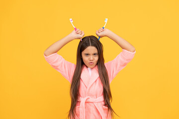 unhappy teen girl in home terry bathrobe hold toothbrush as devils horns, bathroom fun