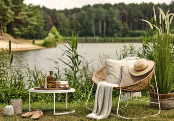 Stylish composition of outdoor garden on the lake with design rattan armchair, coffee table, plaid,...