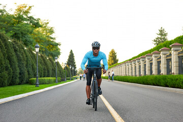 Full length shot of professional male cyclist in sportswear and protective helmet training in the park