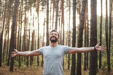 happy Caucasian male in the forest. He spread his arms and closed his eyes. Wellness concept and holistic health practices