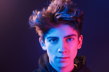 Portrait of young beautiful guy with fashionable haircut. Neon lighting