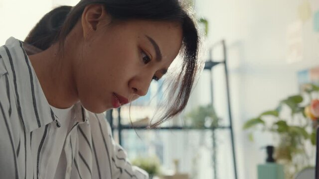 Close-up young asia lady freelance focus mobile phone chat with colleagues work finance graph account chart market plan in laptop at home. Girl student learn online at house, Work from home concept.