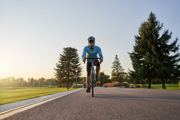Full length shot of professional male cyclist in sportswear and protective helmet training in the park at sunset