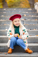 Autumn happy little child in autumn park. Pretty kid girl in a beret and a sweater in autumn warm sunny weather
