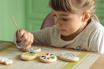 Girl with pigtails paints Easter glazed cookies with a brush while sitting in the kitchen at the...