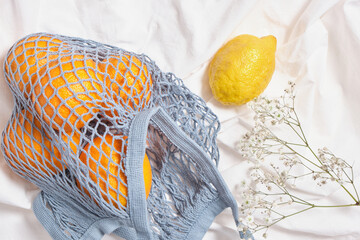 blue mesh eco bag with oranges and lemon on white cloth background