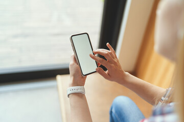 Side view of mockup image of a woman holding smartphone near the window