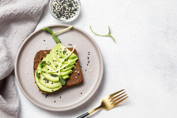 Whole grain rye bread toast with sliced avocado on white stone table background. Healthy avocado open sandwich for breakfast or lunch. Flat lay, top view, copy space