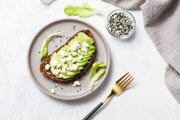Whole grain rye bread toast with goat cheese and avocado on white stone table background. Healthy avocado open sandwich for breakfast or lunch. Flat lay, top view