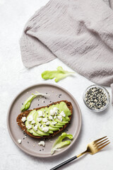 Whole grain rye bread toast with goat cheese and avocado on white stone table background. Healthy avocado open sandwich for breakfast or lunch. Flat lay, top view, copy space