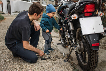Fototapeta na wymiar Father-son communication. A young son and his father are repairing a motorcycle on the street.