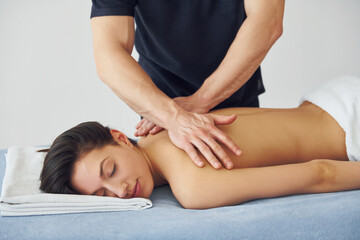 Young woman is lying down when man doing massage of her back at spa