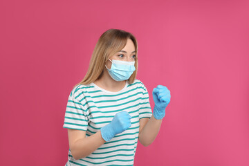 Woman with protective mask and gloves in fighting pose on pink background. Strong immunity concept