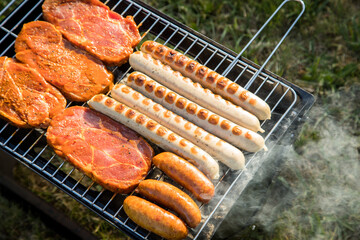 Bratwurst und marinierte Schweine Fleisch Nackensteaks grillen mit Rauch auf Holzkohle Klappgrill im Garten an Sommer Abend