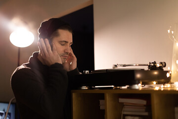 Young unshaven handsome millennial guy listens enjoys to music with headphones closed eyes....