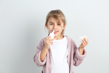 Sick little girl using nasal spray on white background