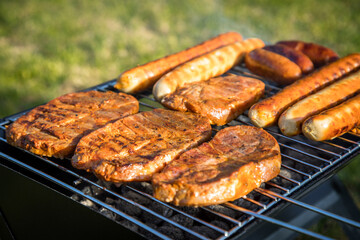 Bratwurst und marinierte Schweine Fleisch Nackensteaks grillen mit Rauch auf Holzkohle Klappgrill im Garten an Sommer Abend