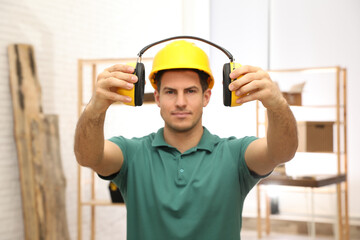 Worker holding safety headphones indoors, focus on hands. Hearing protection device