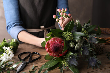 Fototapeta na wymiar Florist making beautiful bouquet with fresh flowers at wooden table, closeup