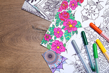 Antistress coloring pages and felt tip pens on wooden table, flat lay. Space for text