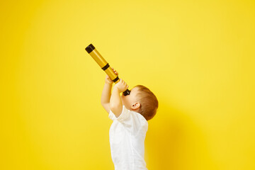 Side view of a child looking through a telescope on a yellow background. The concept of travel, pirates and adventures, active lifestyle, striving for the goal