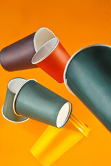 Disposable paper cups fall on an orange background. Glasses of different sizes and colors close up.