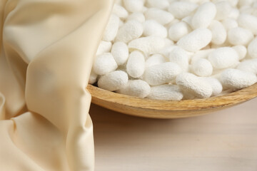 Cocoons with bowl and silk fabric on white wooden table, closeup