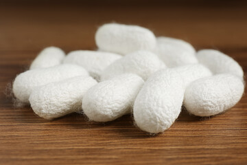 Heap of white silk cocoons on wooden table, closeup