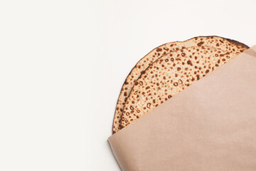 Tasty matzos wrapped with paper on white background, top view. Passover (Pesach) celebration