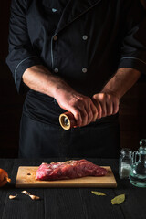 Chef cooking raw meat fillet and adding pepper and chili for marinade on black background. Working environment in kitchen in restaurant or cafe