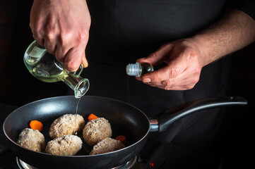 Cooking beef cutlets in a grill pan with the hands of chef or cook on a black background for copying the space text restaurant menu. Chef adds oil