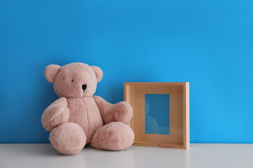 Empty photo frame and teddy bear on white table near light blue wall. Space for design
