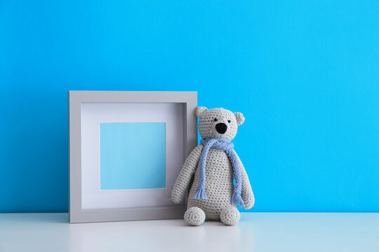 Empty photo frame and toy bear on white table near light blue wall. Space for design