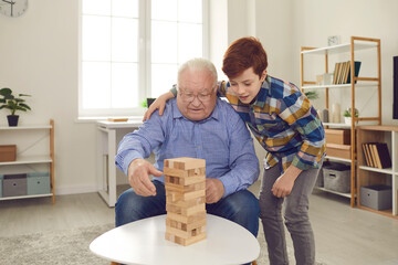 Senior man enjoying board games while spending time with his grandson at home. Supportive little...