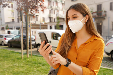 Pretty girl with smartwatch wearing KN95 FFP2 face mask using mobile phone in city street