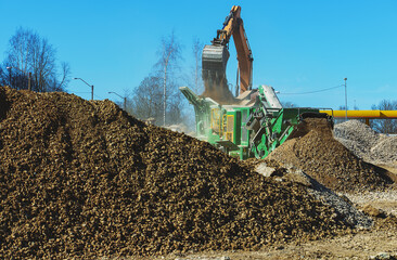 Excavator and screener machine working on construction site.