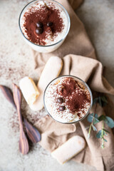 Traditional Italian dessert tiramisu in glass, stone background. Coffee flavored portion dessert made of ladyfingers and mascarpone decorated with cocoa powder. Top view.