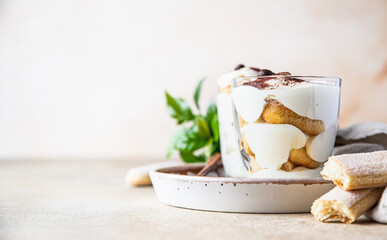 Traditional Italian dessert tiramisu in glass, stone background. Coffee flavored portion dessert made of ladyfingers and mascarpone decorated with cocoa powder.