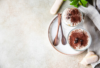 Traditional Italian dessert tiramisu in glass, stone background. Coffee flavored portion dessert made of ladyfingers and mascarpone decorated with cocoa powder. Top view.