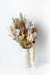Rustic dried flower arrangement in a ceramic white vase. Including Kangaeoo paw, Palm fronds, Native Temp, Ruscus leaves, Stirlingia, Parchment Fern and Amaranthus. Photographed on a white background.