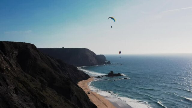 Breathtaking aerial view of Praia da Cordoama in Portugal. It shows paraglider over the beach on a sunny day with a blue sky in the background, as well as the hills of Vila da Bispo.