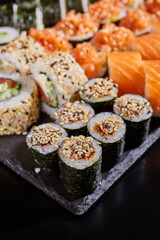 Close up of maki sushi sprinkled with sesame seeds on a stone plate on a dark background.