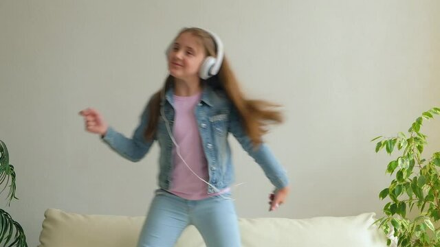 Funny Happy Little Girl in headphones are Dancing and Jump on Couch at Home