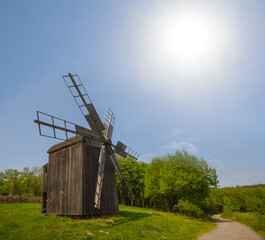 Fototapeta na wymiar wooden authentic windmill among green fields at the sunny day